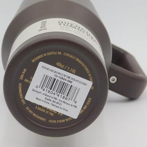 May include: A brown Stanley Quencher tumbler with a handle. The label indicates a 1.18L capacity. The tumbler is designed in Seattle, WA, and ethically manufactured in China. The label also includes a barcode and the text "BPA Free Dishwasher Safe".