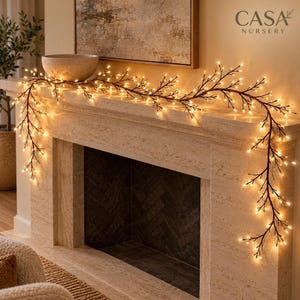 May include: A brown, branch-like garland featuring numerous small, warm white LED lights draped across a stone fireplace mantel. The text CASA NURSERY is visible in the upper right corner of the image above the fireplace mantel.