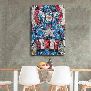 May include: A framed Captain America artwork. The artwork features a collage of comic book images in red, white, and blue, forming the iconic superhero's likeness. The image is displayed on a gray wall above a table with white chairs.
