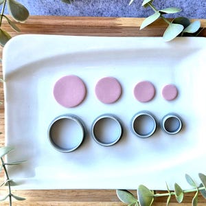 Könnte beinhalten: Ein Set aus drei Keramikbechern mit gesprenkelter, matter Oberfläche. Die Becher sind in Creme-, Hellgrau- und Dunkelgrautönen gehalten. Jeder Becher hat ein schlichtes, minimalistisches Design und einen abgerundeten Henkel.