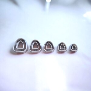 May include: A collection of five grey plastic cookie cutters, each shaped like a nested triangle. The cutters are arranged in a line, with sizes diminishing from left to right. They are set against a white background.