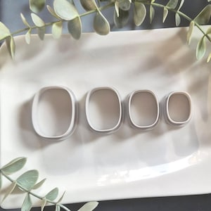 Può includere: Quattro formine bianche, quadrate e arrotondate di diverse dimensioni sono disposte su un piatto rettangolare bianco. Le formine sono nidificate, con la più grande a sinistra e la più piccola a destra. Il verde è visibile sullo sfondo.