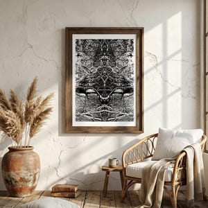 Puede incluir: Una lámina de arte abstracto en blanco y negro enmarcada que presenta un patrón simétrico e intrincado de ramas entrelazadas y líneas orgánicas, expuesta en un marco de madera oscura sobre una pared texturizada encima de una silla de ratán.