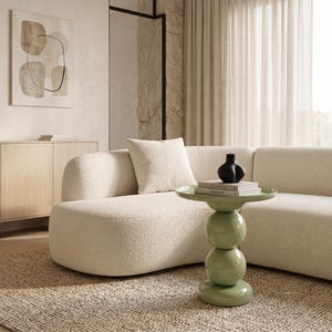 May include: A sage green side table featuring a smooth, glossy finish with a stacked design consisting of two spherical middle sections and a flat circular top, topped with two stacked books and a small black sculptural vase.