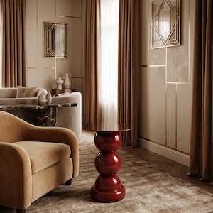 Puede incluir: Una mesa auxiliar de color rojo intenso brillante con un diseño de base apilada de tres segmentos esféricos redondeados que sostienen una superficie circular lisa. La mesa se encuentra sola en una habitación con paredes y cortinas beige.
