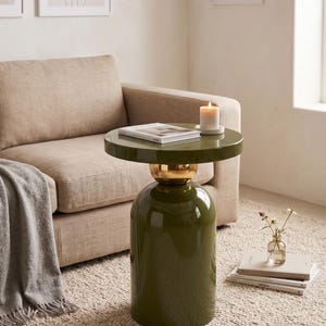 May include: A glossy olive green side table with a cylindrical base and a round top, featuring a polished gold-tone spherical accent connecting the base to the tabletop. The table has a smooth, reflective finish and a sturdy, compact design.