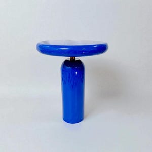 May include: A contemporary blue side table featuring a circular top and a cylindrical base. The table has a glossy finish and a white interior on the tabletop. The table is approximately 50 cm in height and 38 cm in diameter.