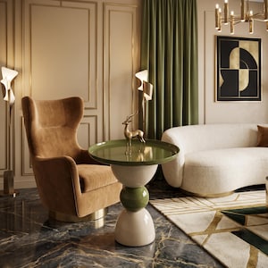 Puede incluir: Una mesa auxiliar redonda con una superficie verde oliva brillante y una base apilada compuesta por un hemisferio color crema, una esfera verde oliva más pequeña y una base color crema más grande, con una figura de ciervo dorada.