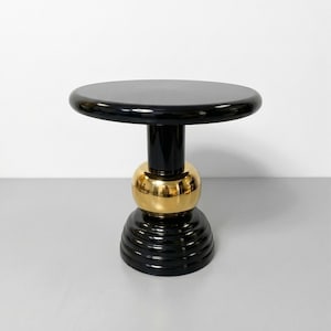 Puede incluir: Una mesa auxiliar moderna con una parte superior y una base redondas negras. La mesa presenta una esfera dorada en el medio, agregando un toque de lujo. La mesa mide aproximadamente 51 cm de altura.