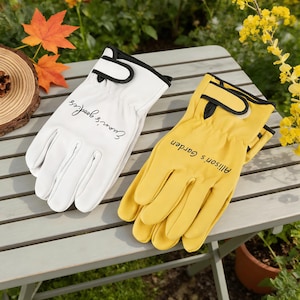 May include: Two gardening gloves, one white and one yellow, with black trim. The white glove has the text "Evan's goodies" and the yellow glove has the text "Allison's Garden". They rest on a grey wooden table.