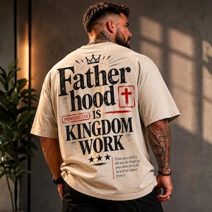 Peut inclure: Un t-shirt beige à manches courtes avec le texte noir Fatherhood is KINGDOM WORK, une icône de croix rouge et le texte Proverbs 22:6. Sous le texte, trois étoiles apparaissent au-dessus du verset : Train up a child in the way he should go.