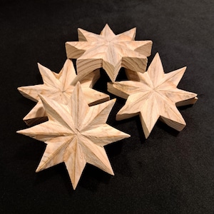 Peut inclure: Plusieurs ornements en forme d'étoiles en bois non fini. Chaque étoile à huit branches est sculptée avec des lignes détaillées. Les étoiles sont disposées sur une surface noire, idéales pour les projets de bricolage.