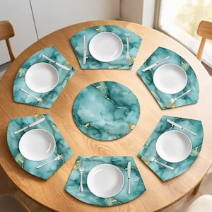 May include: A set of six teal and gold marble-patterned placemats arranged on a round wooden table. Each placemat features a white ceramic plate, a silver fork, and a silver knife. A matching circular placemat is positioned in the center.