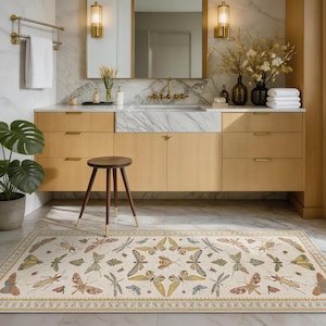 May include: A rectangular beige rug with a repeating pattern of insects and leaves in shades of green, yellow, brown, and gray. The rug is placed in a bathroom with light wood cabinets, a marble countertop, and a small wooden stool.