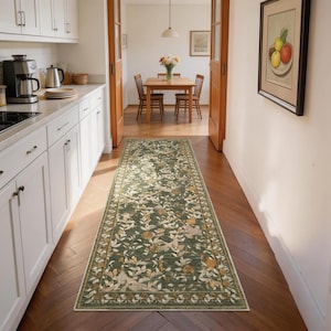 May include: A long, rectangular green rug with a floral pattern, placed in a hallway. The rug features a dark green background with cream and yellow floral and leaf designs. The rug is bordered with a cream and green trim. The hallway has a wooden floor.