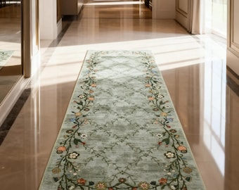 May include: A rectangular, light green runner rug with a floral border. The rug features a repeating diamond pattern in the center and a detailed border of colorful flowers and leaves. The rug is placed in a hallway with a polished floor.