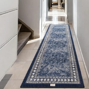 May include: A long, rectangular blue rug with a distressed pattern and a white diamond border. The rug is placed in a hallway with white walls and tile flooring. The rug's dimensions are not visible.