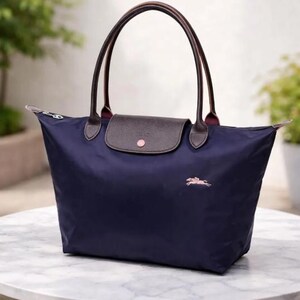 Puede incluir: Bolso tote azul marino con asas de cuero marr&oacute;n y cierre de solapa. El bolso presenta un logotipo rosa de un caballo corriendo y un bot&oacute;n rosa en la solapa. El bolso es de nailon.