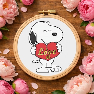 May include: A cross-stitch embroidery hoop featuring Snoopy holding a red heart with the words "Love U" in yellow. The design is set against a white background, framed by a wooden hoop. Pink peonies surround the hoop.