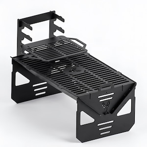 May include: A black metal portable barbecue with a slotted cooking surface and a separate grill grate. The barbecue has a deer head logo and a handle. Designed for outdoor cooking.