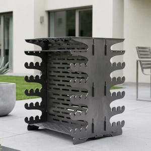 Puede incluir: Un leñero de metal gris oscuro con un diseño abierto único. El soporte tiene forma rectangular con recortes decorativos y ranuras horizontales para ventilación. Los lados tienen un patrón de árbol y la base es sólida.