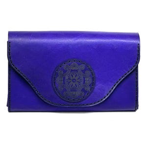 May include: A vibrant purple leather wallet with a decorative circular embossed design on the front flap. The wallet features a curved flap closure and is stitched with dark thread. The overall design is simple and elegant.