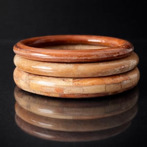 Peut inclure: Trois bracelets en bois empilés, dans des tons de marron et de beige. Le bracelet supérieur est d'un brun foncé riche, tandis que celui du milieu est d'un beige plus clair. Le bracelet inférieur a un motif en mosaïque.