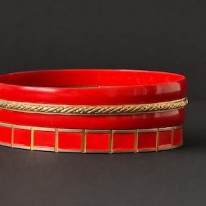 Conjunto de brazaletes apilables de esmalte rojo vintage en tono dorado, joyería llamativa de los años 80 con aspecto lacado.