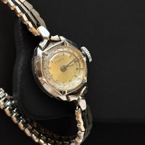 May include: A vintage Timex watch with a silver case and a gold-coloured face. The watch has a silver, linked band. The watch face displays the Timex brand name. A classic timepiece.
