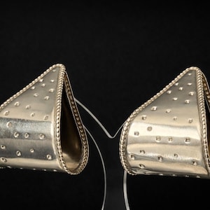 May include: A pair of silver-toned earrings with a triangular shape. The earrings have a textured surface with small, evenly spaced indentations and a rope-like border. They are displayed against a black background.