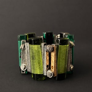 May include: A wide cuff bracelet constructed from alternating vertical segments of translucent lime green and dark emerald green glass, interspersed with textured silver and bronze metal bars secured by small circular rivets and metal pins.