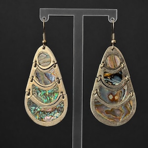 May include: A pair of teardrop-shaped earrings featuring a metallic frame with a distressed finish. Each earring is composed of four stacked, crescent-shaped segments inlaid with iridescent abalone shell pieces in shades of green, blue, and brown.