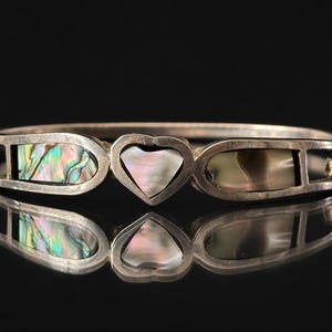 Peut inclure: Bracelet articulé argenté avec incrustations d'ormeau irisé et un cœur central. Le bracelet présente des incrustations rectangulaires et en forme de cœur, avec une surface réfléchissante en dessous.
