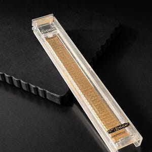May include: A gold-toned watch band in a clear plastic case. The band is made of small, rectangular links. The case has the brand name "Kreisler" printed on it. The watch band is 12mm wide.
