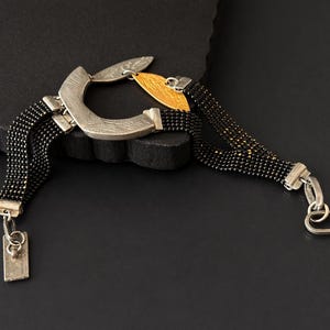 May include: A silver and black beaded bracelet with a unique design. The bracelet features a curved silver centerpiece with gold accents and multiple strands of black beads. The clasp is silver.