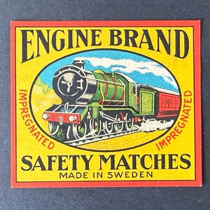 May include: A square matchbox label featuring a green and black steam locomotive illustration inside an oval. The text reads ENGINE BRAND, SAFETY MATCHES, MADE IN SWEDEN, and IMPREGNATED. The background is yellow with a red border.