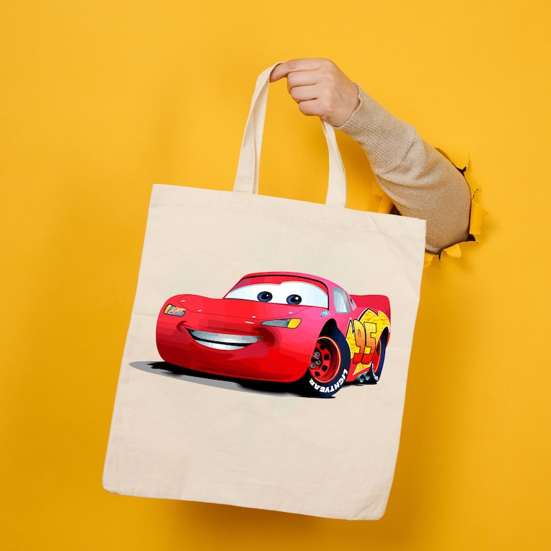Op de afbeelding: Een beige draagtas met een kleurrijke illustratie van Lightning McQueen, een rode raceauto met nummer 95 en gele accenten. De tas heeft twee handvatten en een eenvoudig ontwerp.