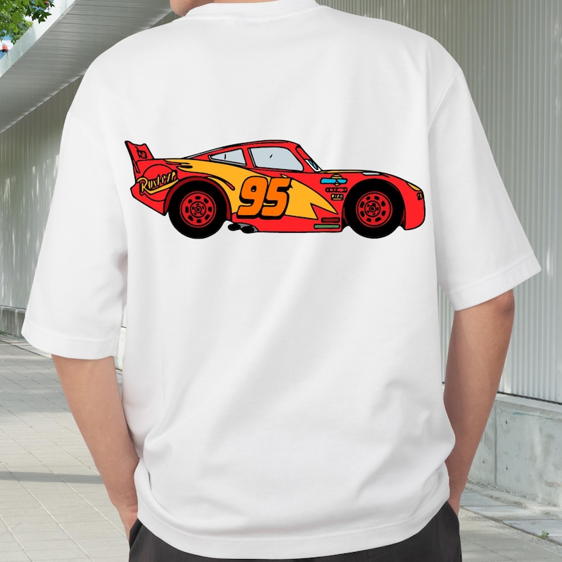 Op de afbeelding: Wit T-shirt met een kleurrijke cartoon illustratie van een rood-gele raceauto met nummer 95. Het auto-ontwerp bevat het woord "Rusteze" en zwarte wielen. Dit is een casual kledingstuk.