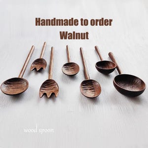 May include: Handmade walnut wood spoons and forks are displayed on a white surface. The spoons have a deep bowl shape, and the forks have three tines. The text "Handmade to order Walnut" and "wood spoon" are visible.