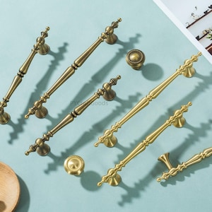 May include: An assortment of antique brass cabinet hardware, including handles and knobs. The hardware features ornate detailing and a warm, aged finish. The handles vary in size and design, suitable for various furniture pieces.