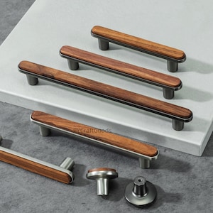 May include: A selection of cabinet handles and knobs. The hardware features rectangular pulls with dark wood and silver-coloured metal accents, plus a round knob and a T-shaped knob. The wood has a natural grain pattern.