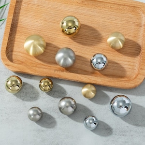 May include: A collection of decorative cabinet knobs in various metallic finishes, including gold, silver, and chrome. The knobs are spherical and arranged on a wooden tray, offering a range of sizes and styles for home decor projects.
