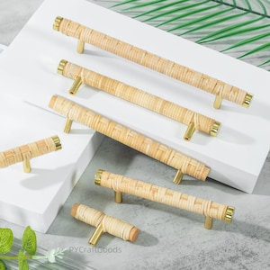 May include: A selection of woven rattan cabinet pulls with brass fittings. The pulls are in various sizes and shapes, with a natural, light brown colour. The fittings are a shiny gold colour. The pulls are arranged on a white surface.
