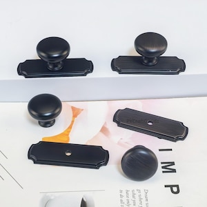 May include: A collection of black cabinet knobs and pulls. The knobs are round and sit atop rectangular backplates with decorative edges. Some pieces are separated, showing the hardware's components. The text "PYCraftGoods" is visible on one of the backplates.
