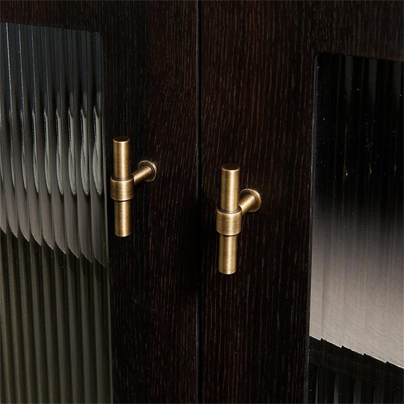 K&ouml;nnte beinhalten: Nahaufnahme eines dunkelbraunen Holzschranks mit zwei T&uuml;ren. Jede T&uuml;r hat einen messingfarbenen Griff. Die Schrankt&uuml;ren haben eine strukturierte Glasscheibe. Die Holzmaserung ist sichtbar.