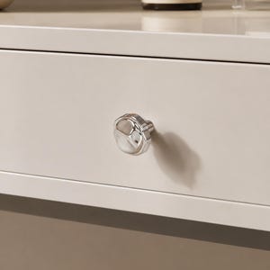 May include: Close-up of a light beige drawer with a silver, faceted knob. The knob has a rounded, irregular shape and reflects the light. The drawer is part of a larger piece of furniture.