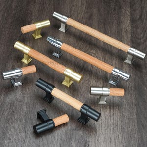 May include: A collection of cabinet pulls with wooden handles and metal accents. The pulls feature a variety of finishes, including gold, silver, and black. The wooden handles have a natural wood grain finish. The pulls are arranged on a dark wood surface.