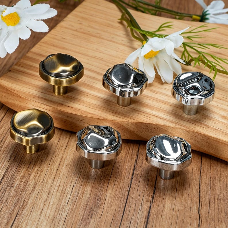 May include: Six decorative cabinet knobs in two styles. Three knobs have a brushed brass finish, and three are polished silver. The knobs have a unique, textured design and are mounted on short stems.