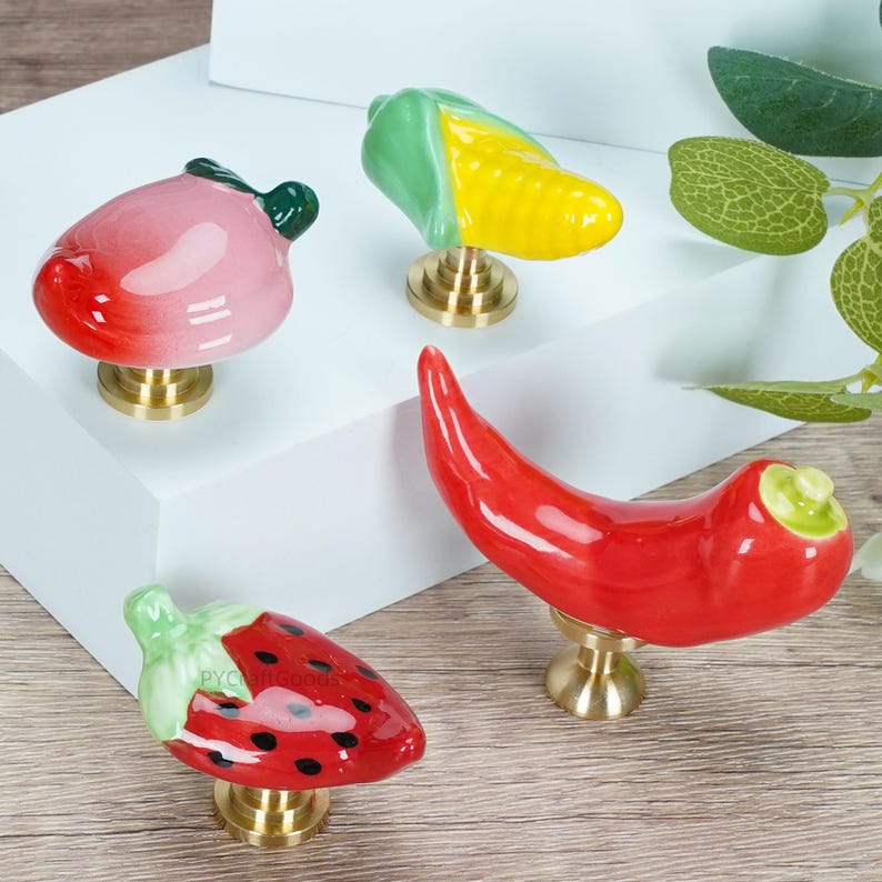 Pode incluir: Uma cole&ccedil;&atilde;o de puxadores de arm&aacute;rio de cer&acirc;mica em forma de frutas e vegetais. O conjunto inclui um p&ecirc;ssego, milho, pimenta vermelha e um morango. Cada puxador tem uma base de lat&atilde;o e &eacute; pintado &agrave; m&atilde;o com cores vibrantes.