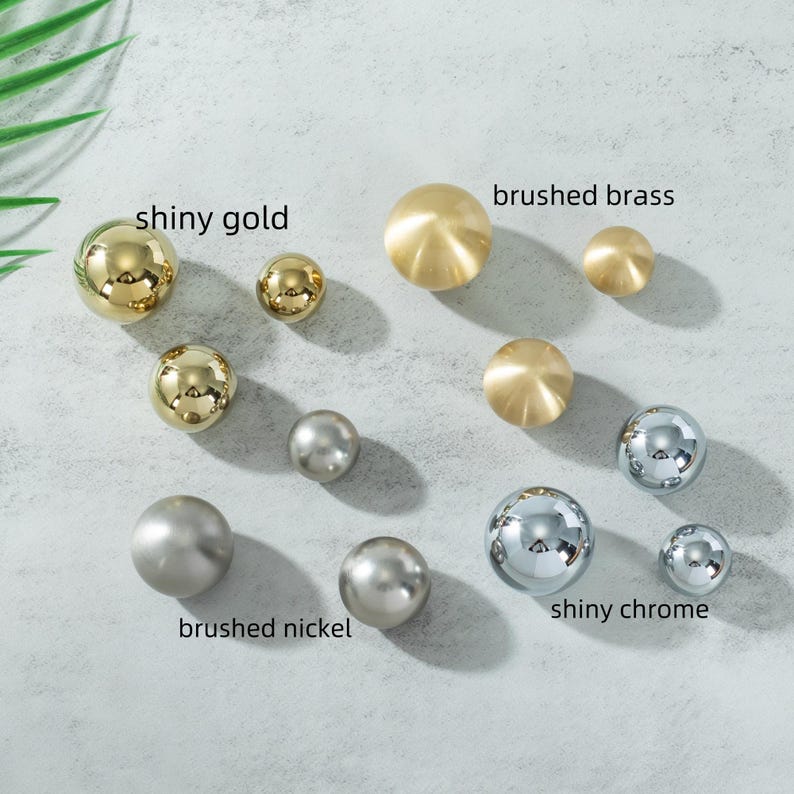 K&ouml;nnte beinhalten: Eine Auswahl an dekorativen, kugelf&ouml;rmigen Kn&ouml;pfen in verschiedenen Ausf&uuml;hrungen. Die Ausf&uuml;hrungen umfassen gl&auml;nzendes Gold, geb&uuml;rstetes Messing, geb&uuml;rstetes Nickel und gl&auml;nzendes Chrom. Text kennzeichnet jede Ausf&uuml;hrung. Diese Kn&ouml;pfe sind f&uuml;r M&ouml;bel oder Schr&auml;nke.